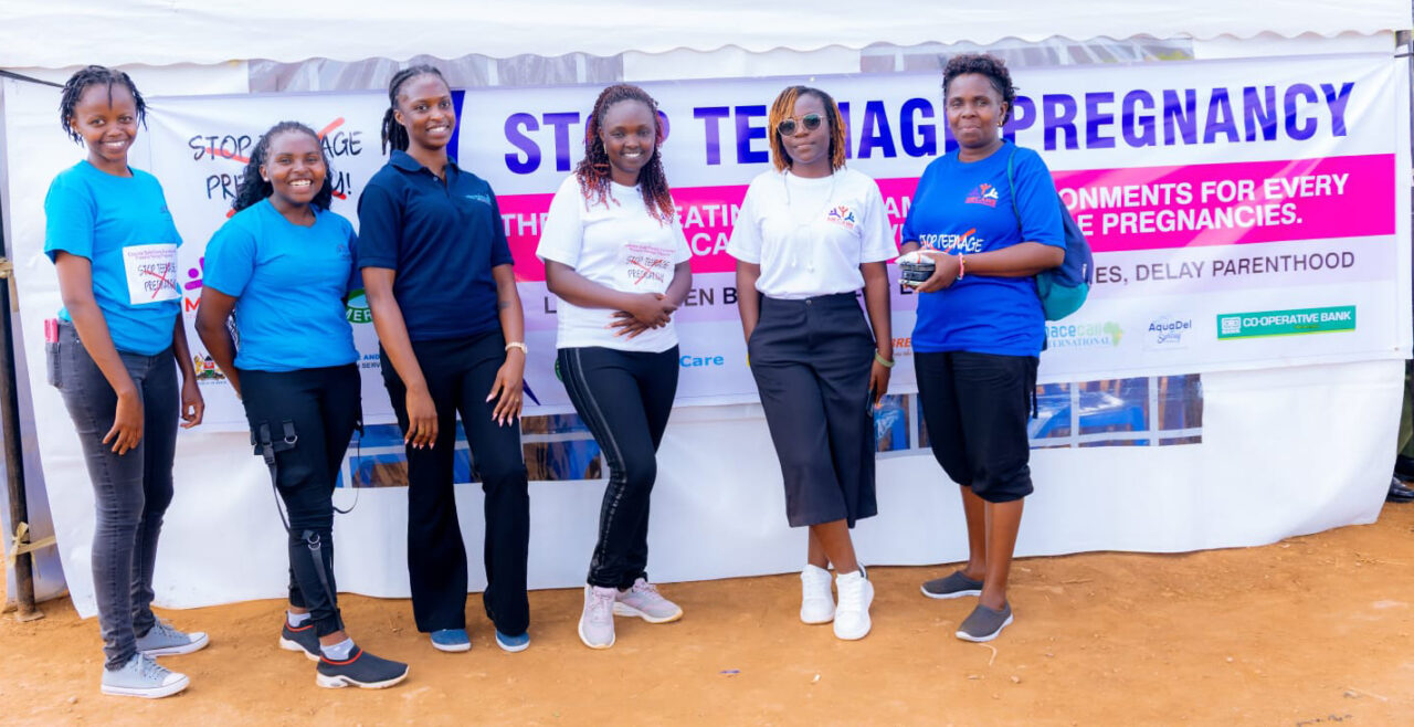 Mary Nakate with other community members standing in front of a 'Stop Teenage Pregnancy' sign
